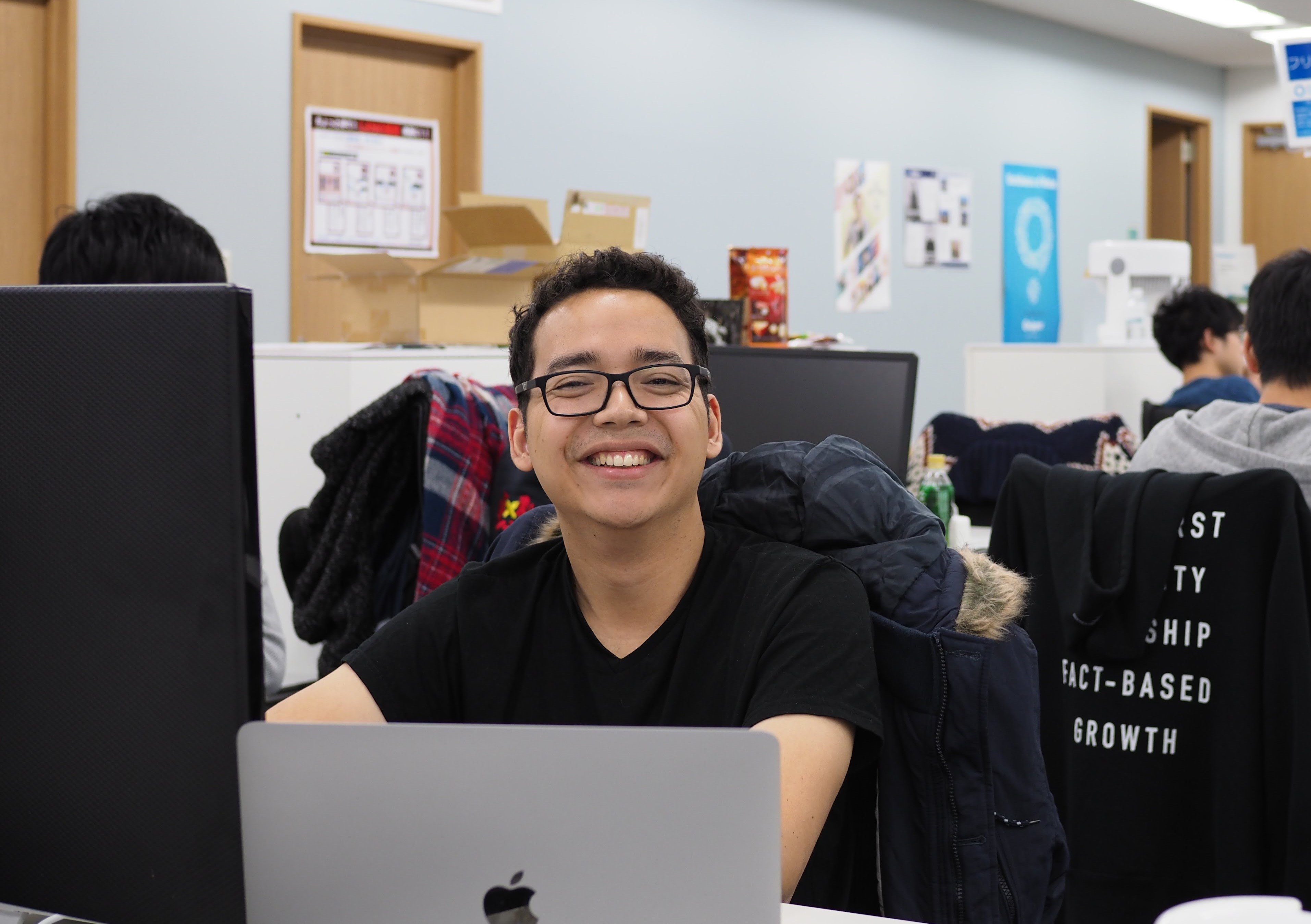 Davi Nakano smiling to the camera while sitting on a chair inside of an office space