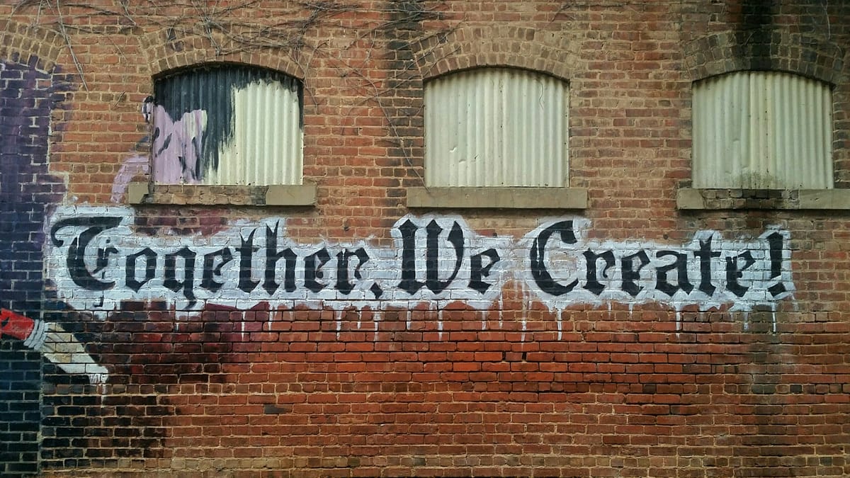 A graffiti on a brick wall displaying the text "Together We Create!"